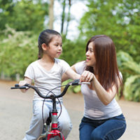 Asian mother teaching little girl to ride a bike