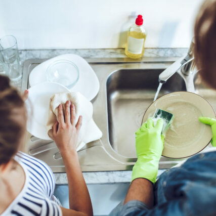 Top view of young happy couple is washing dishes while doing cleaning at home.